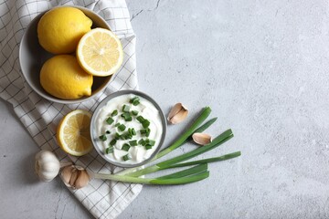 Delicious yogurt, green onion, garlic and lemons on light textured table, flat lay. Space for text