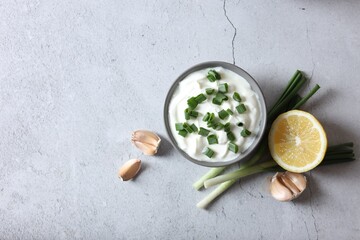 Delicious yogurt, green onion, garlic and lemons on light textured table, flat lay. Space for text