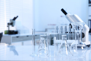 Laboratory analysis. Different glassware and microscope on white table indoors, space for text