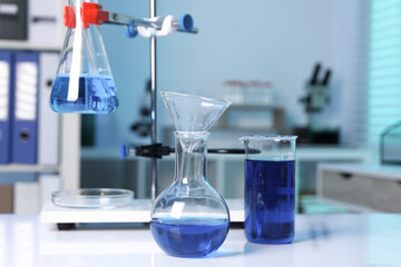 Laboratory analysis. Flasks and beaker with blue liquid on white table indoors