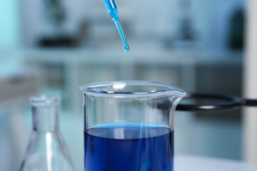Laboratory analysis. Dripping blue liquid into beaker on table, closeup
