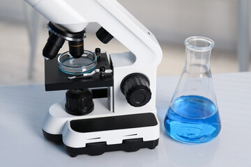 Laboratory analysis. Flask with blue liquid, petri dish and microscope on white table indoors