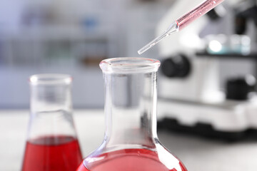 Laboratory analysis. Dripping red liquid into flask at light grey table, closeup