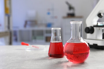 Laboratory analysis. Flasks with red liquid, petri dish and microscope on light grey table