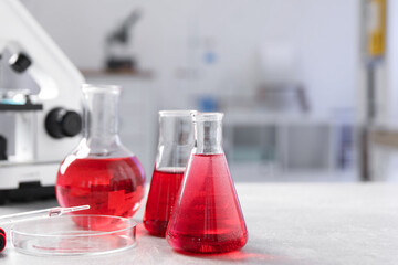 Laboratory analysis. Different flasks with red liquid and microscope on light grey table indoors