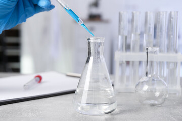 Laboratory analysis. Woman dripping liquid into flask at light grey table, closeup