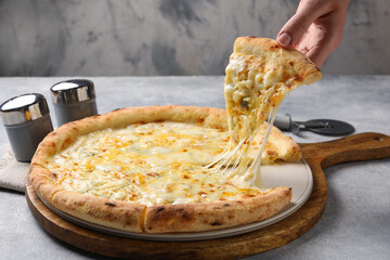 Woman taking piece of delicious cheese pizza at light grey table, closeup