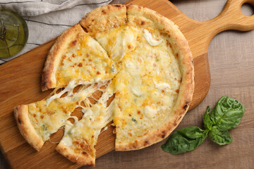 Delicious cut cheese pizza, basil and oil on wooden table, flat lay