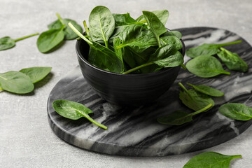 Fresh spinach leaves in bowl on light textured table, closeup