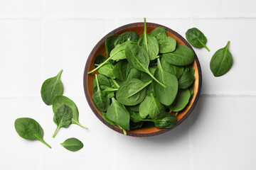 Fresh spinach leaves in bowl on white tiled table, flat lay