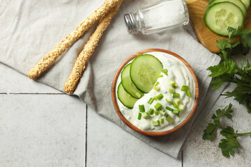 Delicious yogurt with green onion, cucumbers, parsley and grissini on light tiled table, top view
