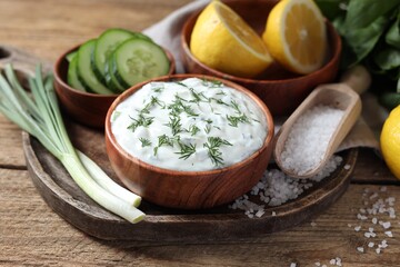 Delicious yogurt, green onion, cucumbers, salt and lemon on wooden table, closeup