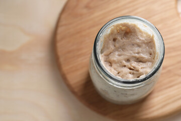 Sourdough starter in glass jar on wooden table, top view. Space for text