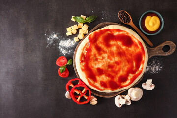 Pizza dough smeared with tomato sauce and products on dark table, flat lay. Space for text