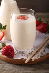Tasty yogurt in glass, straws and strawberries on wooden table, closeup