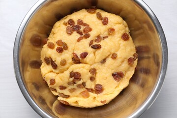 Dough with raisins in bowl on white wooden table, top view