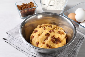 Dough with raisins in bowl and ingredients on white wooden table
