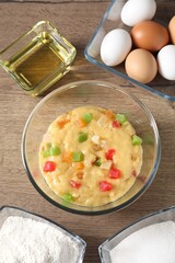 Raw dough with candied fruits in bowl and ingredients on wooden table, flat lay