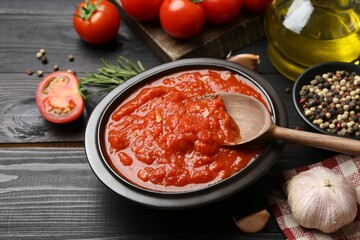 Homemade tomato sauce in bowl, spoon and fresh ingredients on black wooden table