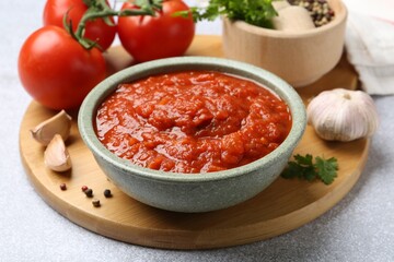Homemade tomato sauce in bowl and fresh ingredients on light grey table, closeup