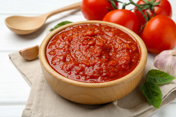 Homemade tomato sauce in bowl, spoon and fresh ingredients on white wooden table, closeup