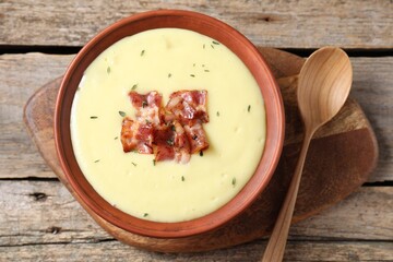 Tasty potato soup with bacon in bowl and spoon on wooden table, flat lay