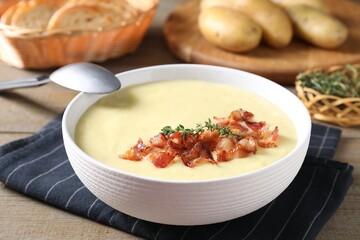 Tasty potato soup with bacon and rosemary in bowl served on wooden table