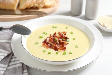 Tasty potato soup with bacon in bowl and spoon on white table
