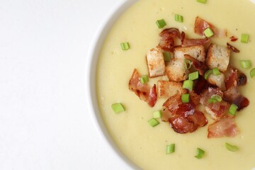 Tasty potato soup with bacon, green onion and croutons in bowl on white table, top view. Space for text