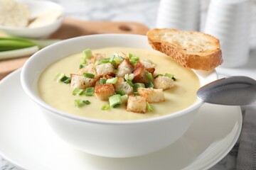 Tasty potato soup with croutons in bowl and spoon on white table