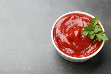 Delicious tomato ketchup and parsley in bowl on grey textured table, closeup. Space for text