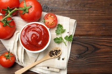 Delicious ketchup in bowl, tomatoes, parsley and peppercorns on wooden table, top view. Space for text