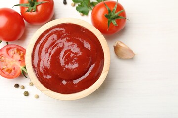 Delicious ketchup in bowl, peppercorns and tomatoes on white wooden table, flat lay. Space for text