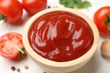 Delicious ketchup in bowl and tomatoes on white table, closeup