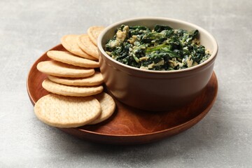 Tasty spinach dip with egg and crackers on grey table, closeup
