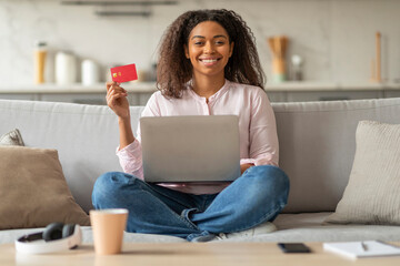 Smiling woman holding credit card while shopping online with laptop