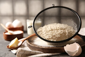 Making dough. Flour in sieve, spoon and butter on grey table, closeup