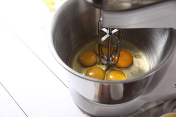 Making dough. Raw eggs in bowl of stand mixer on white table, closeup