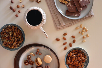 Cup of tea or coffee, cookies, macaroons, chocolate, various nuts and cocoa powder on white background. Top view.