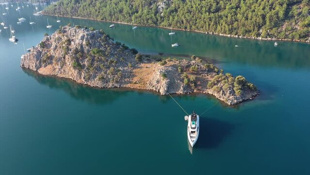 A mega yacht moored at small island. Turning around yacht anchored in aquaclear water. Castle ruins on top of island located in middle of bay in Orhaniye, Marmaris belongs to ancient city of Baybassos