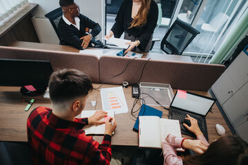 A mixed group of young professionals engage in project discussions and analysis in a stylish, well-equipped office setting, demonstrating teamwork and dedication.