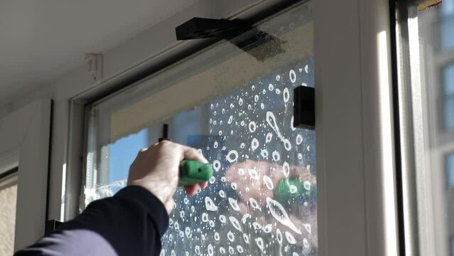 Worker installing and smoothing tint film on window at home. Man tinting windows with squeegee