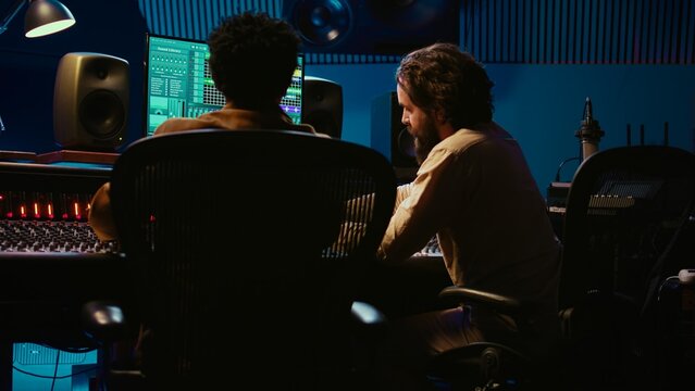 Audio expert and musician mixing and mastering tracks on control room console in studio, recording and editing tunes in music post production. Skilled artist and sound engineer. Camera B.