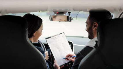 Arabic male driving instructor accepts a test from Caucasian female student during practical test. View from the back seat of the car