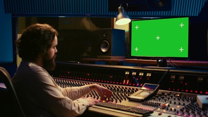 Audio expert editing tracks by following online lesson on greenscreen pc, mixing new tunes together to create a song. Sound engineer working in control room to record and process music. Camera B.