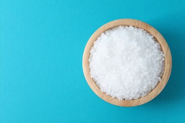 Organic white salt in bowl on light blue background, top view. Space for text