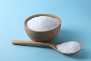 Organic white salt in bowl and spoon on light blue background