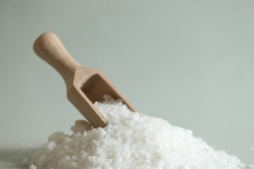 Organic salt and wooden scoop on light grey background, closeup. Space for text