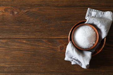 Organic salt in bowl on wooden table, top view. Space for text