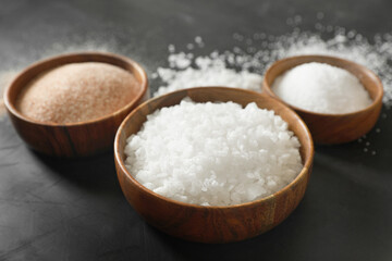 Different types of organic salt in bowls on black table, closeup